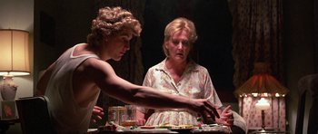 Movie still from “At Close Range” (1986), directed by James Foley – Two people sitting at a dinner table with food and drinks; Medium shot, Over the shoulder angle
