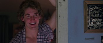 Movie still from “At Close Range” (1986), directed by James Foley – A young man smiling for the camera while leaning against a wall; Close Up shot, Low angle
