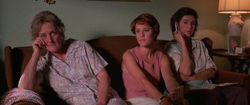 Movie still from “At Close Range” (1986), directed by James Foley – A woman sitting next to two other women on a couch; Medium shot, High angle