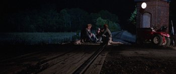 Movie still from “At Close Range” (1986), directed by James Foley – Three people sitting on a train track at night; Wide shot, High angle