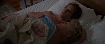 Movie still from “At Close Range” (1986), directed by James Foley – A man and a woman laying in a bed together; Medium shot, High angle