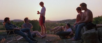 Movie still from “At Close Range” (1986), directed by James Foley – A group of people sitting and standing on the ground; Wide shot, Low angle