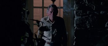 Movie still from “At Close Range” (1986), directed by James Foley – An older man standing in front of a window at night; Medium shot, Low angle