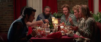 Movie still from “At Close Range” (1986), directed by James Foley – A group of people sitting around a table eating; Medium shot, Over the shoulder angle