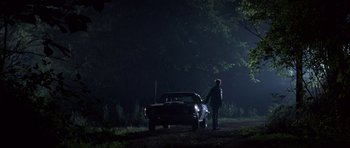 Movie still from “At Close Range” (1986), directed by James Foley – A man standing next to a car in the dark; Wide shot, Low angle