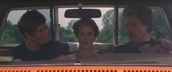 Movie still from “At Close Range” (1986), directed by James Foley – A woman sitting in the driver's seat of an orange car; Close Up shot, Over the shoulder angle