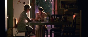 Movie still from “At Close Range” (1986), directed by James Foley – Two women sitting at a table in front of a window; Wide shot, Over the shoulder angle