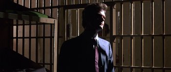 Movie still from “At Close Range” (1986), directed by James Foley – A man wearing a suit and tie standing in front of a jail cell; Close Up shot, Low angle