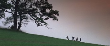 Movie still from “At Close Range” (1986), directed by James Foley – A group of people walking up a grassy hill; Extreme Wide shot, Low angle