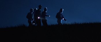 Movie still from “At Close Range” (1986), directed by James Foley – A group of people walking on a field at night; Wide shot, High angle