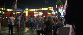 Movie still from “At Close Range” (1986), directed by James Foley – A group of people walking around a carnival at night; Wide shot, High angle