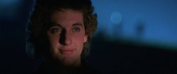 Movie still from “At Close Range” (1986), directed by James Foley – A young man is smiling for the camera in the dark; Close Up shot, Low angle