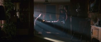Movie still from “At Close Range” (1986), directed by James Foley – A group of people sitting around a table in a room; Wide shot, Over the shoulder angle