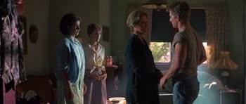 Movie still from “At Close Range” (1986), directed by James Foley – A group of people standing in a living room talking; Medium shot, Over the shoulder angle