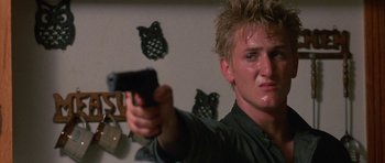 Movie still from “At Close Range” (1986), directed by James Foley – A man holding a gun in a room with owl decorations on the wall; Close Up shot, Low angle
