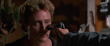 Movie still from “At Close Range” (1986), directed by James Foley – A man is holding a gun up to his face; Close Up shot, Over the shoulder angle