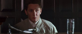 Movie still from “At Close Range” (1986), directed by James Foley – A man sitting in front of a microphone in front of a microphone; Close Up shot, Over the shoulder angle