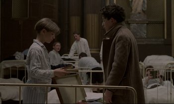 Movie still from “Au revoir les enfants” (1987), directed by Louis Malle – A man and a woman looking at something on a book; Medium shot, High angle
