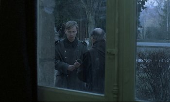 Movie still from “Au revoir les enfants” (1987), directed by Louis Malle – A man is looking at his cell phone in a mirror; Medium shot, Over the shoulder angle