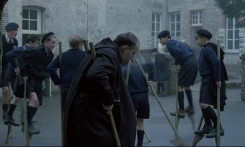 Movie still from “Au revoir les enfants” (1987), directed by Louis Malle – A group of people standing around each other with brooms; Wide shot, High angle