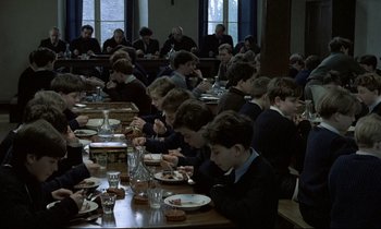 Movie still from “Au revoir les enfants” (1987), directed by Louis Malle – A group of people sitting at a table eating food; Wide shot, High angle