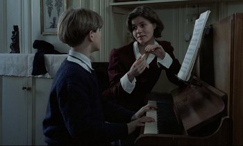 Movie still from “Au revoir les enfants” (1987), directed by Louis Malle – A woman teaching a young boy how to play piano; Medium shot, Over the shoulder angle