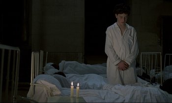Movie still from “Au revoir les enfants” (1987), directed by Louis Malle – A person standing in front of two lit candles on a bed; Medium shot, High angle