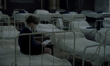 Movie still from “Au revoir les enfants” (1987), directed by Louis Malle – A person sitting on a bed reading a book; Wide shot, High angle