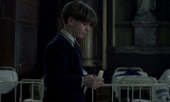 Movie still from “Au revoir les enfants” (1987), directed by Louis Malle – A young boy holding a cell phone while standing next to a railing; Medium shot, Over the shoulder angle