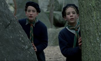 Movie still from “Au revoir les enfants” (1987), directed by Louis Malle – Two young boys wearing hats and ties standing next to a tree; Medium shot, High angle