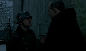 Movie still from “Au revoir les enfants” (1987), directed by Louis Malle – A man in a helmet and a man in a coat and tie; Medium shot, Over the shoulder angle