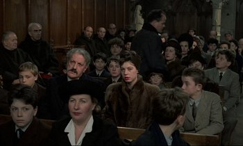 Movie still from “Au revoir les enfants” (1987), directed by Louis Malle – A group of people sitting in a room; Medium shot, High angle