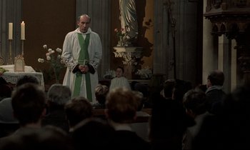Movie still from “Au revoir les enfants” (1987), directed by Louis Malle – A priest is standing in front of a group of people; Medium shot, Low angle