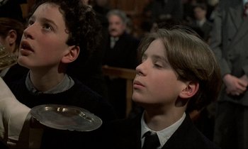Movie still from “Au revoir les enfants” (1987), directed by Louis Malle – Two young men in suits and ties in front of an audience; Medium shot, Low angle