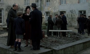 Movie still from “Au revoir les enfants” (1987), directed by Louis Malle – A group of people standing around in a courtyard; Wide shot, Over the shoulder angle