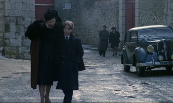 Movie still from “Au revoir les enfants” (1987), directed by Louis Malle – A woman and a boy walking down a street; Wide shot, Over the shoulder angle
