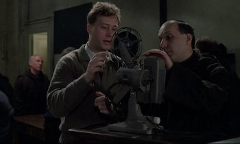 Movie still from “Au revoir les enfants” (1987), directed by Louis Malle – Two men looking at a film projector in a room; Medium shot, Low angle