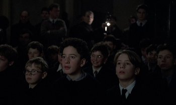 Movie still from “Au revoir les enfants” (1987), directed by Louis Malle – A group of young men sitting next to each other in a room; Medium shot, High angle