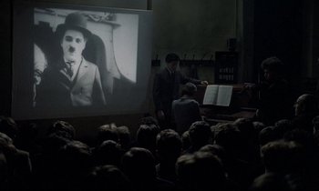 Movie still from “Au revoir les enfants” (1987), directed by Louis Malle – An audience is watching a movie with charlie chaplin on the screen; Medium shot, High angle