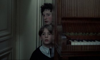 Movie still from “Au revoir les enfants” (1987), directed by Louis Malle – Two young boys standing in front of a piano; Medium shot, High angle