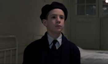 Movie still from “Au revoir les enfants” (1987), directed by Louis Malle – A young boy wearing a hat and a tie; Close Up shot, High angle