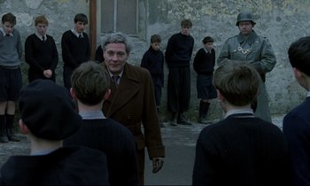 Movie still from “Au revoir les enfants” (1987), directed by Louis Malle – A group of young men standing around a man in a brown suit; Medium shot, Over the shoulder angle