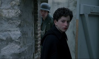 Movie still from “Au revoir les enfants” (1987), directed by Louis Malle – Two young men in uniforms are standing in an alleyway; Medium shot, Over the shoulder angle