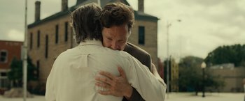 Movie still from “August: Osage County” (2013), directed by John Wells – Two men hugging each other in front of a brick building; Close Up shot, Over the shoulder angle