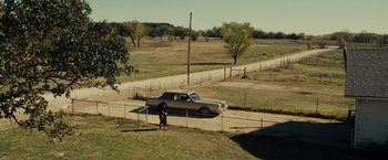 Movie still from “August: Osage County” (2013), directed by John Wells – A dog standing next to a car on the side of the road; Extreme Wide shot, High angle