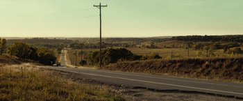 Movie still from “August: Osage County” (2013), directed by John Wells – An empty road in the middle of a field with power lines overhead; Extreme Wide shot, High angle