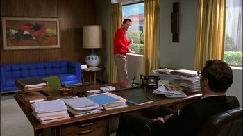 Movie still from “Auto Focus” (2002), directed by Paul Schrader – A man standing in front of a window in a cluttered room; Wide shot, Over the shoulder angle