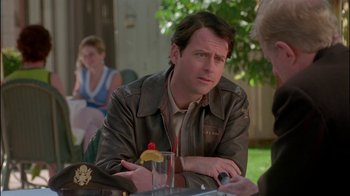 Movie still from “Auto Focus” (2002), directed by Paul Schrader – A man sitting at an outdoor table with a drink in front of him; Medium shot, Over the shoulder angle