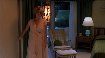 Movie still from “Auto Focus” (2002), directed by Paul Schrader – A woman standing in front of a window in a room; Medium shot, Low angle