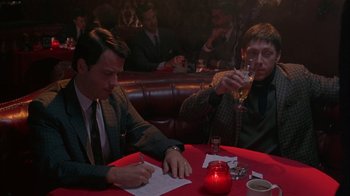 Movie still from “Auto Focus” (2002), directed by Paul Schrader – Two men sitting at a table in front of a glass of wine; Medium shot, Over the shoulder angle